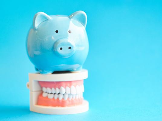Blue piggy bank atop model teeth representing the cost of dental emergencies