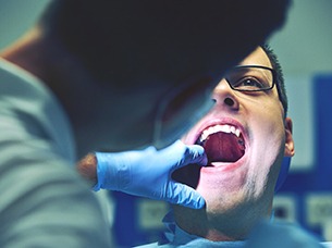 emergency dentist inspecting patient’s smile 