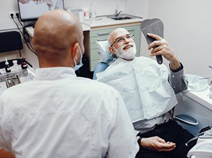 senior man admiring his smile after getting dental implant restorations placed 