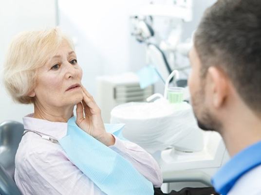 senior woman with a toothache talking to her emergency dentist in Arlington 