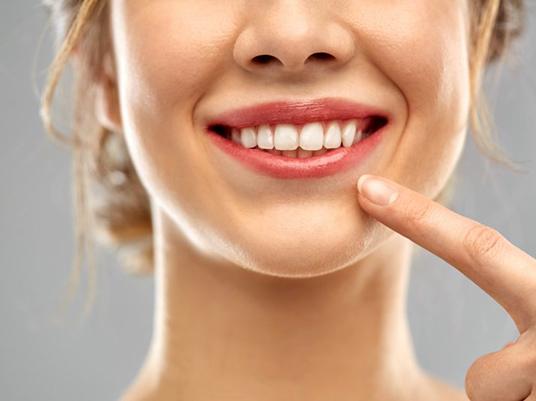 close up woman pointing to smile after in-office teeth whitening in Arlington 