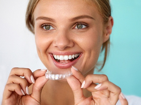 A woman holding an orthodontic clear aligner.