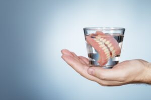 Hand holding glass of water with dentures soaking in it.